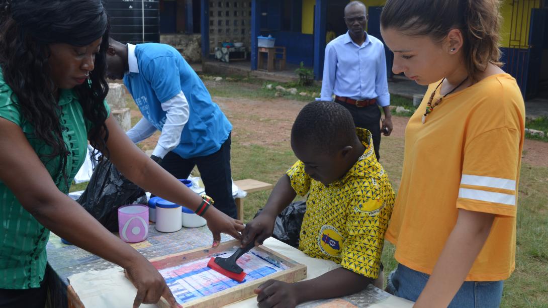 Gap year volunteers work in Ghana with children as part of the year-long trip. A teacher and volunteer in Ghana assist a child with an art project on a gap year program abroad.